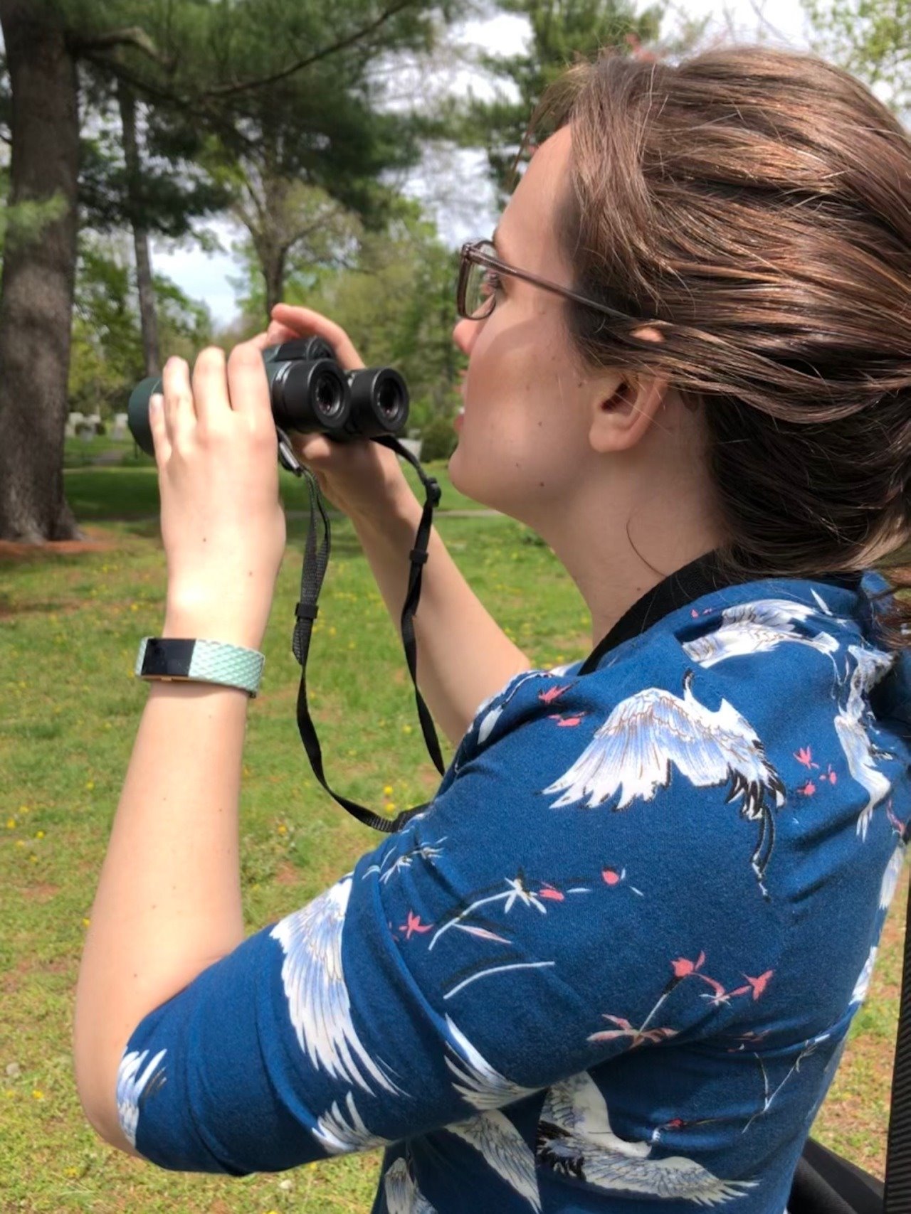 Rebecca Doris looking through binoculars away from the camera at Mount Auburn Cemetery in Cambridge.